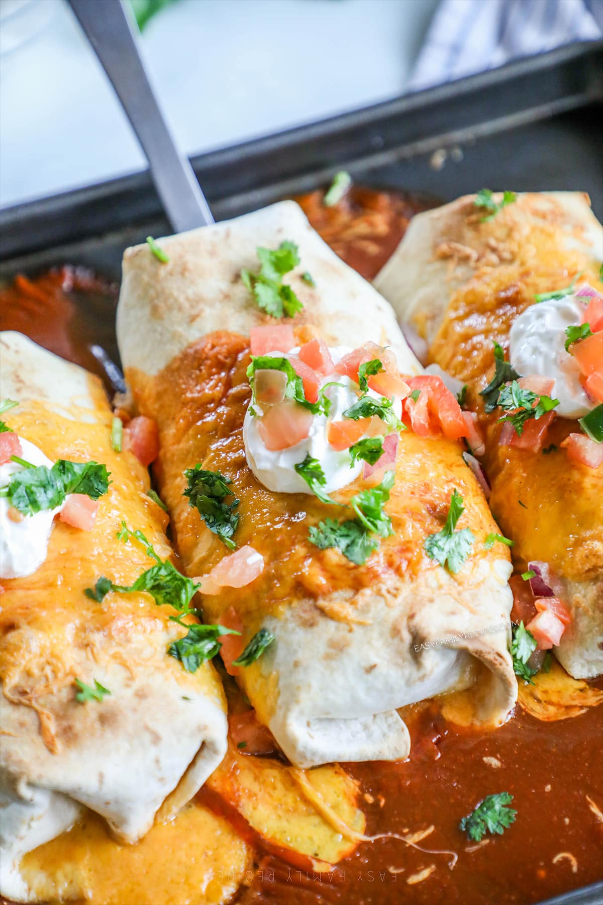 Baked chicken chimichangas on a baking sheet with sour cream and cilantro. 