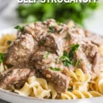 A white plate full of beef stroganoff over pasta with parsley in the background. The text reads, "Crockpot Beef Stroganoff."