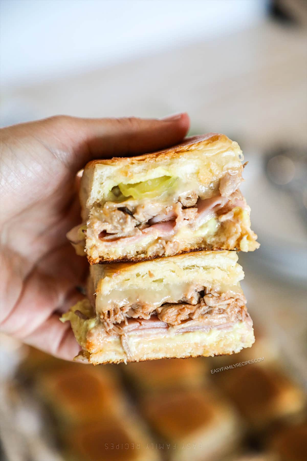 A hand holds two Hawaiian Roll Cuban Sliders.