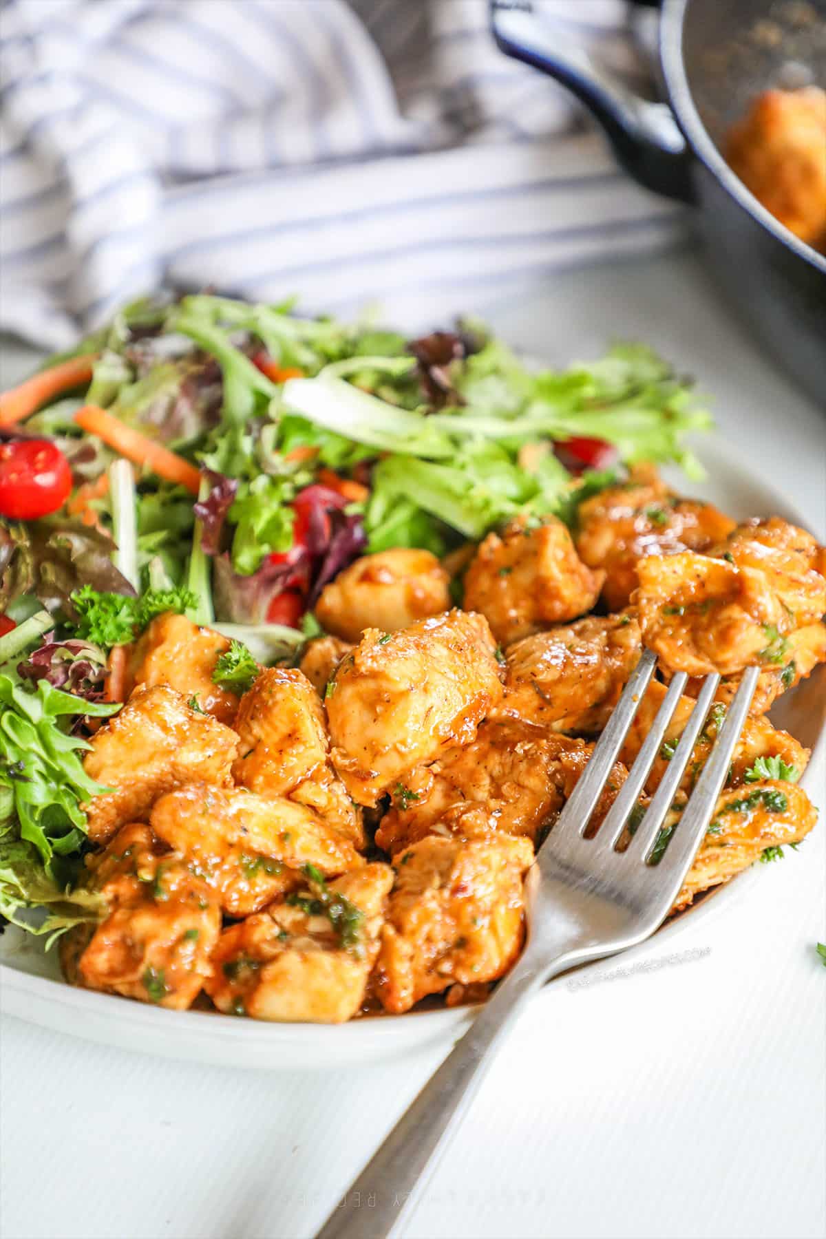 Garlic Butter Chicken Bites served on a white plate with a green salad. A silver fork is perched on the side.