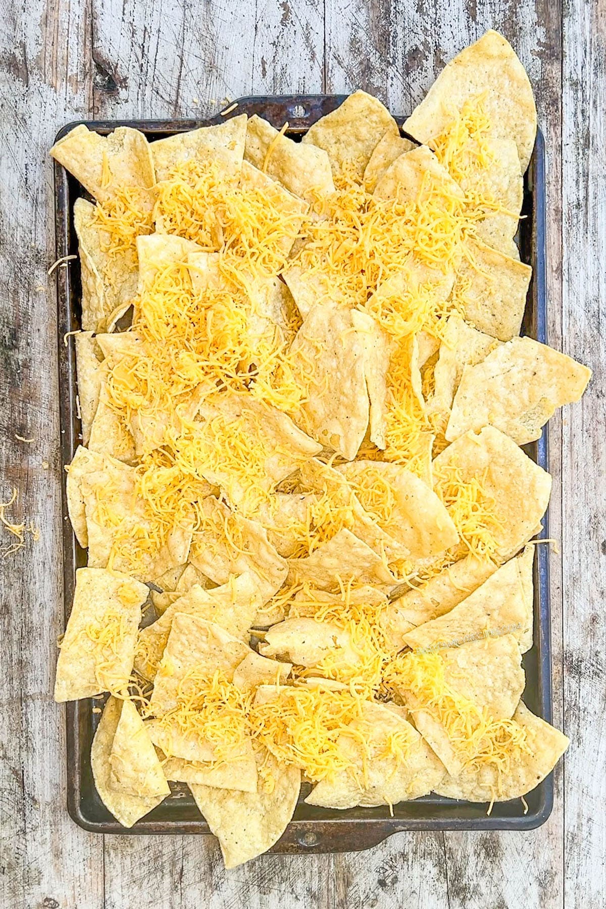 A layer of tortilla chips on a sheet pan, step 1 of making BBQ chicken nachos.