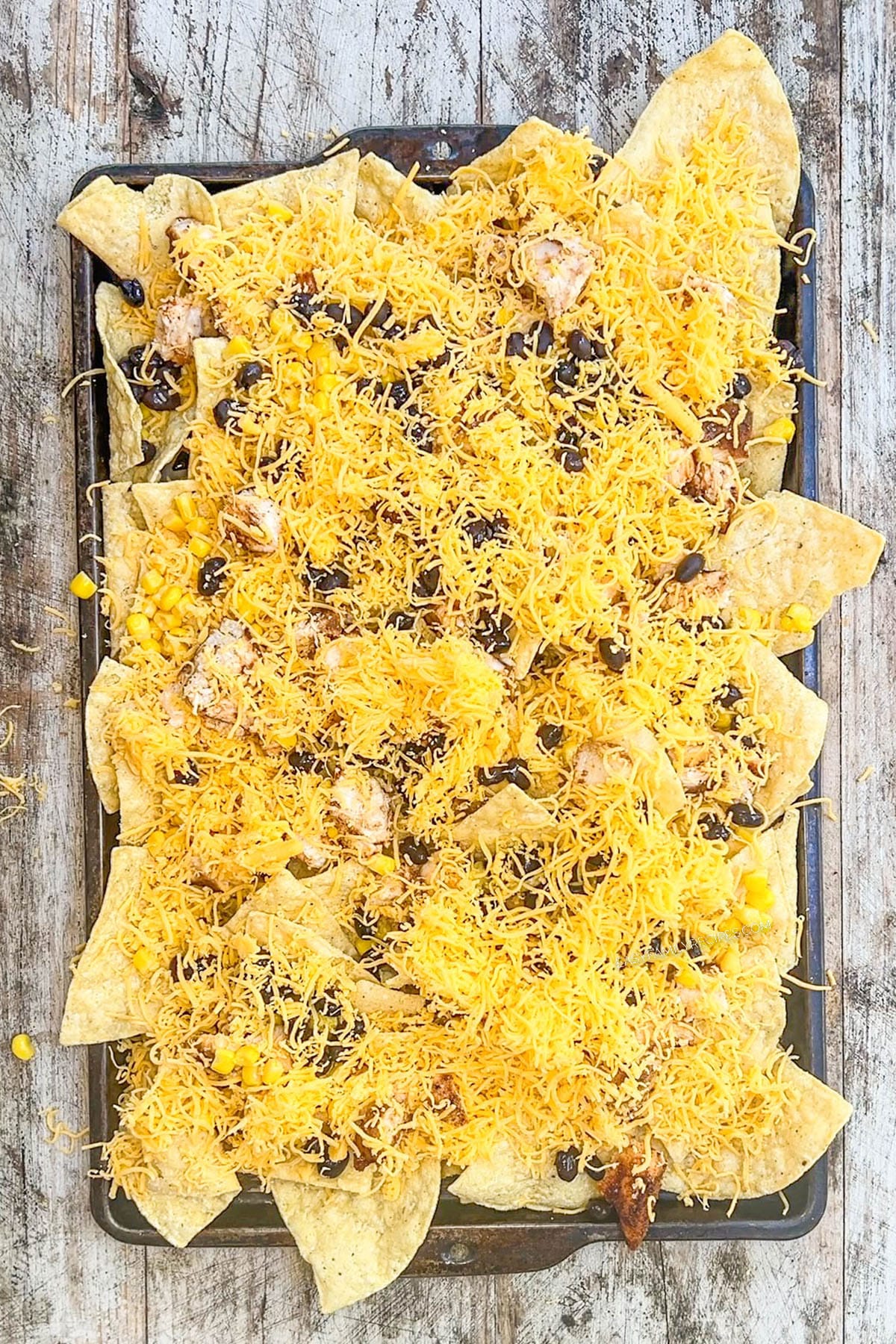 Cheese is added to tortilla chips in a baking pan, step 4 of how to make BBQ chicken nachos.