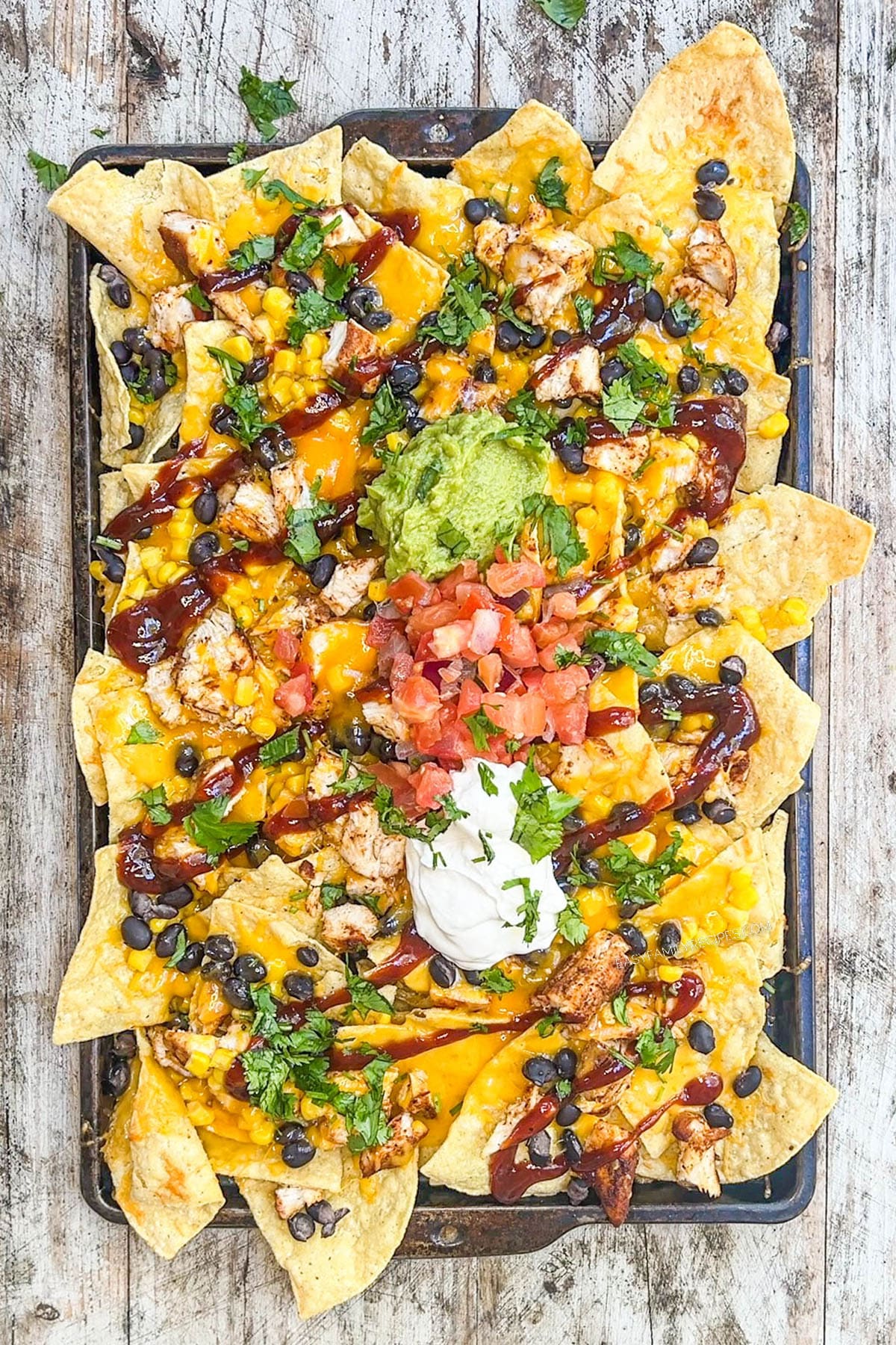 Toppings are added to the baking sheet full of BBQ chicken nachos, which is step 6 of how to make the nachos.