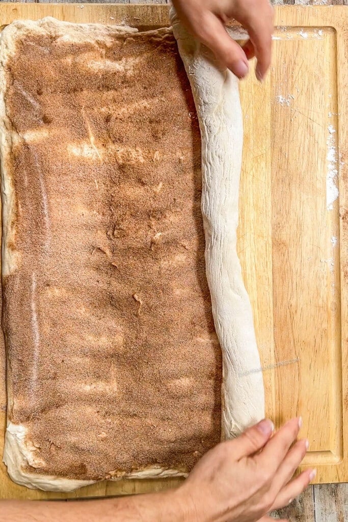 dough topped with cinnamon and sugar being rolled up.