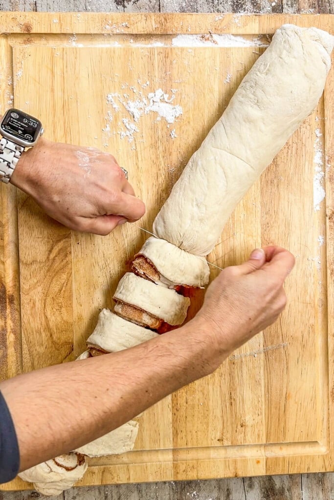 a large roll of cinnamon roll dough being cut into smaller rolls.