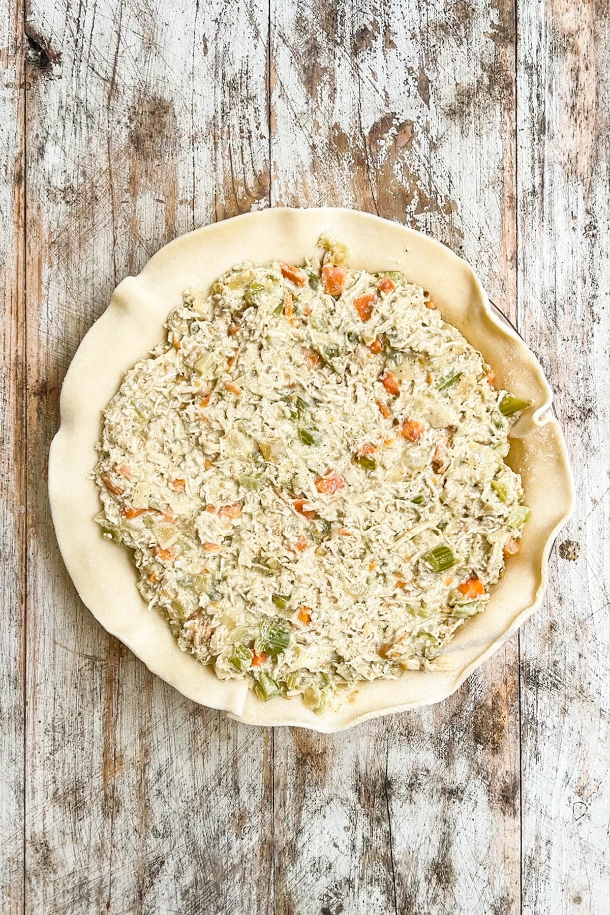 Step 5 of making chicken pot pie: The filling is added to the pie plate, on top of the first layer of pie crust.