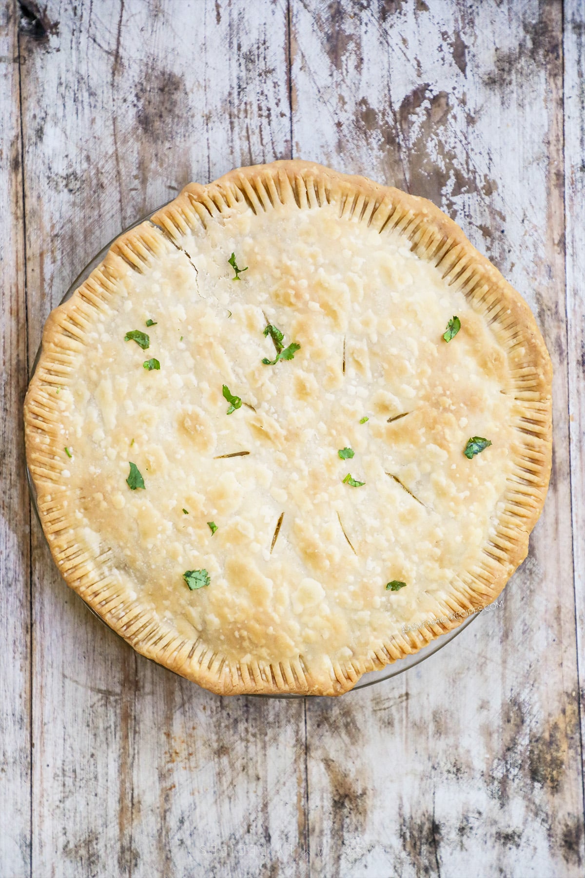 Step 6 of making easy chicken pot pie: The baked pot pie with parsley garnish on top, on a distressed wood background.