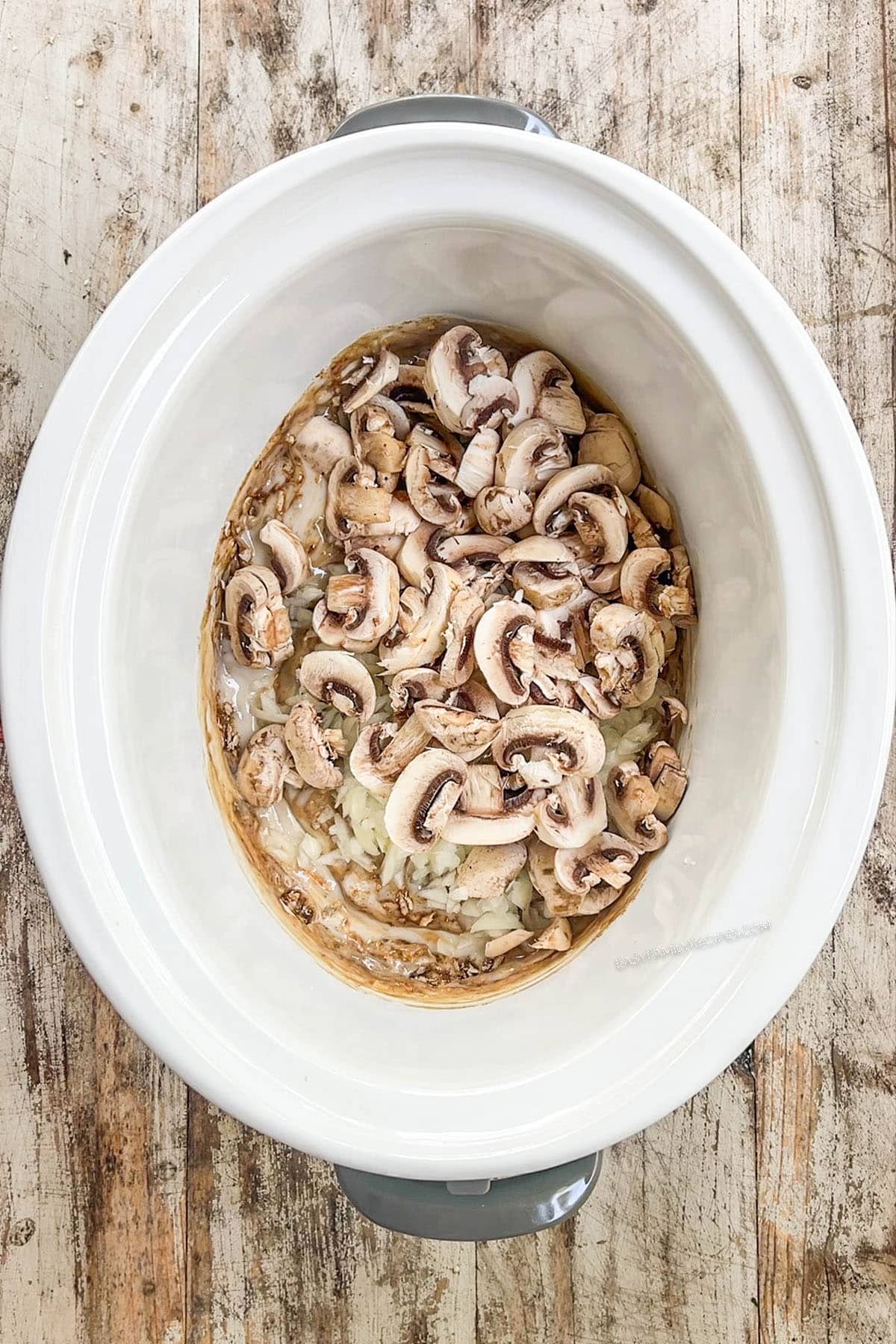 Mushrooms are added to a white Crock Pot for stroganoff.