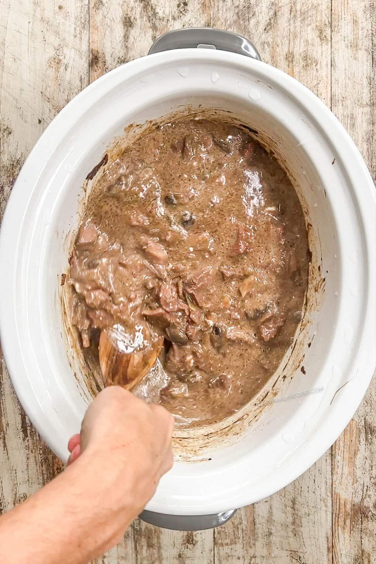 Step 6 of making beef stroganoff, mixing in the sour cream. The stroganoff is in a white Crock Pot.