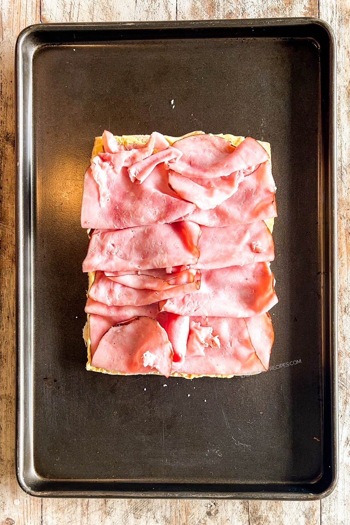 Ham is placed on top of the rolls while making Hawaiian Roll Cuban Sliders.