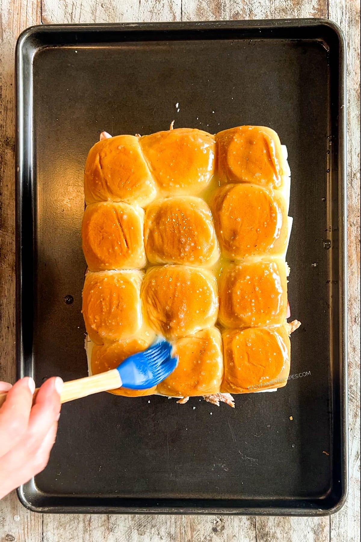 The top layer of rolls is placed on top of Hawaiian Roll Cuban Sliders and brushed with garlic butter.