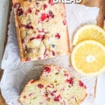 above image of a loaf of orange cranberry bread on a cutting board with orange slices.