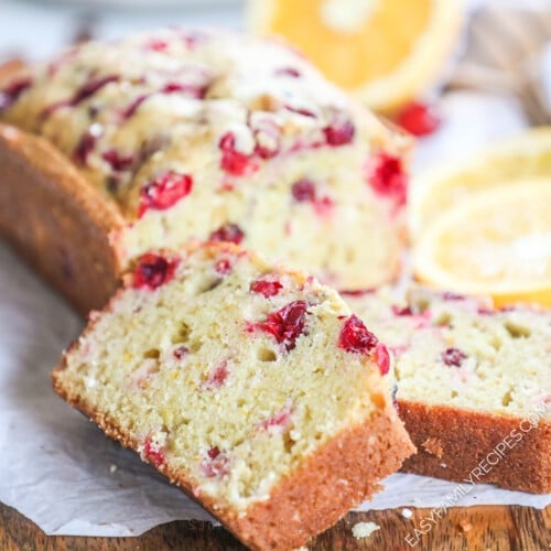 a loaf of cranberry orange bread on a cutting board with two slices cut off.