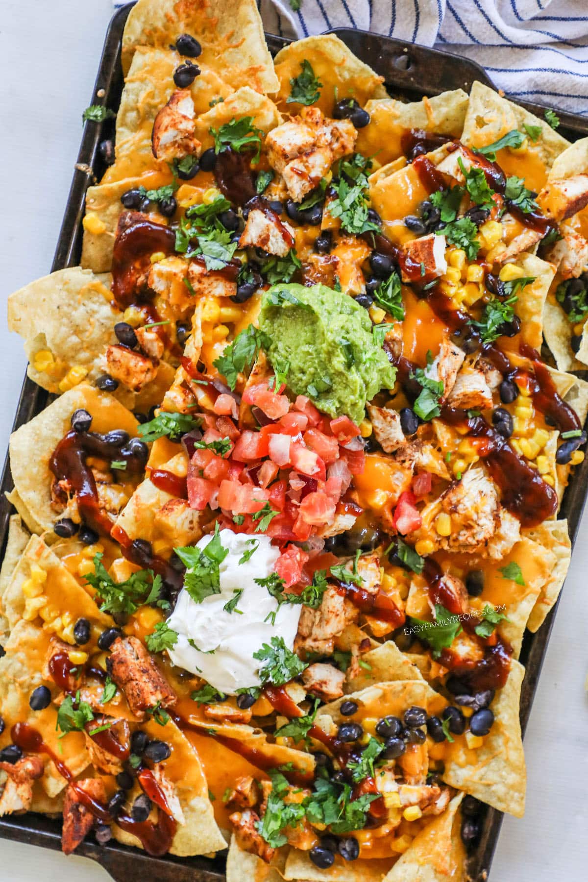 A sheet pan full of BBQ chicken nachos with assorted toppings. 