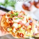 A hand holds up a BBQ Chicken Tostada. The text reads, "BBQ Chicken Tostadas."