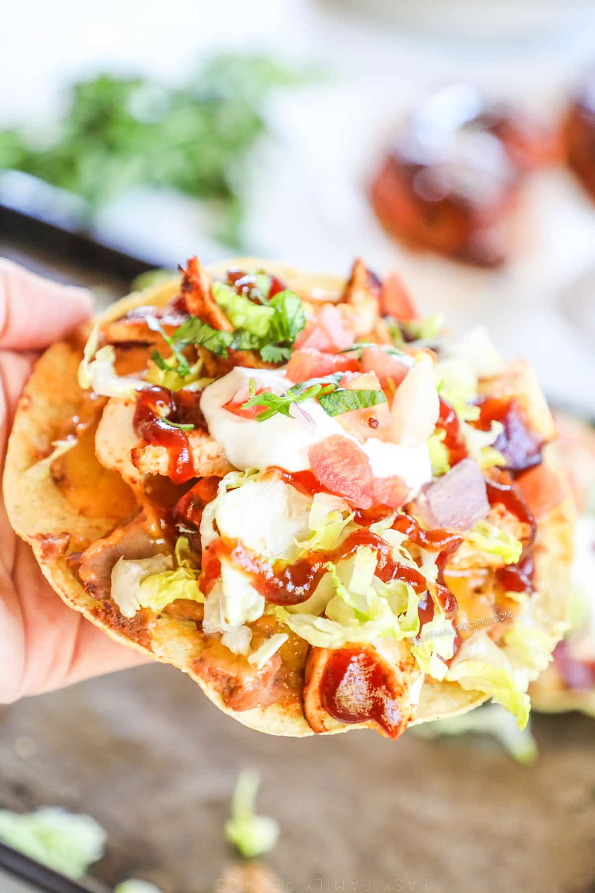 A hand holds up a BBQ Chicken Tostada.