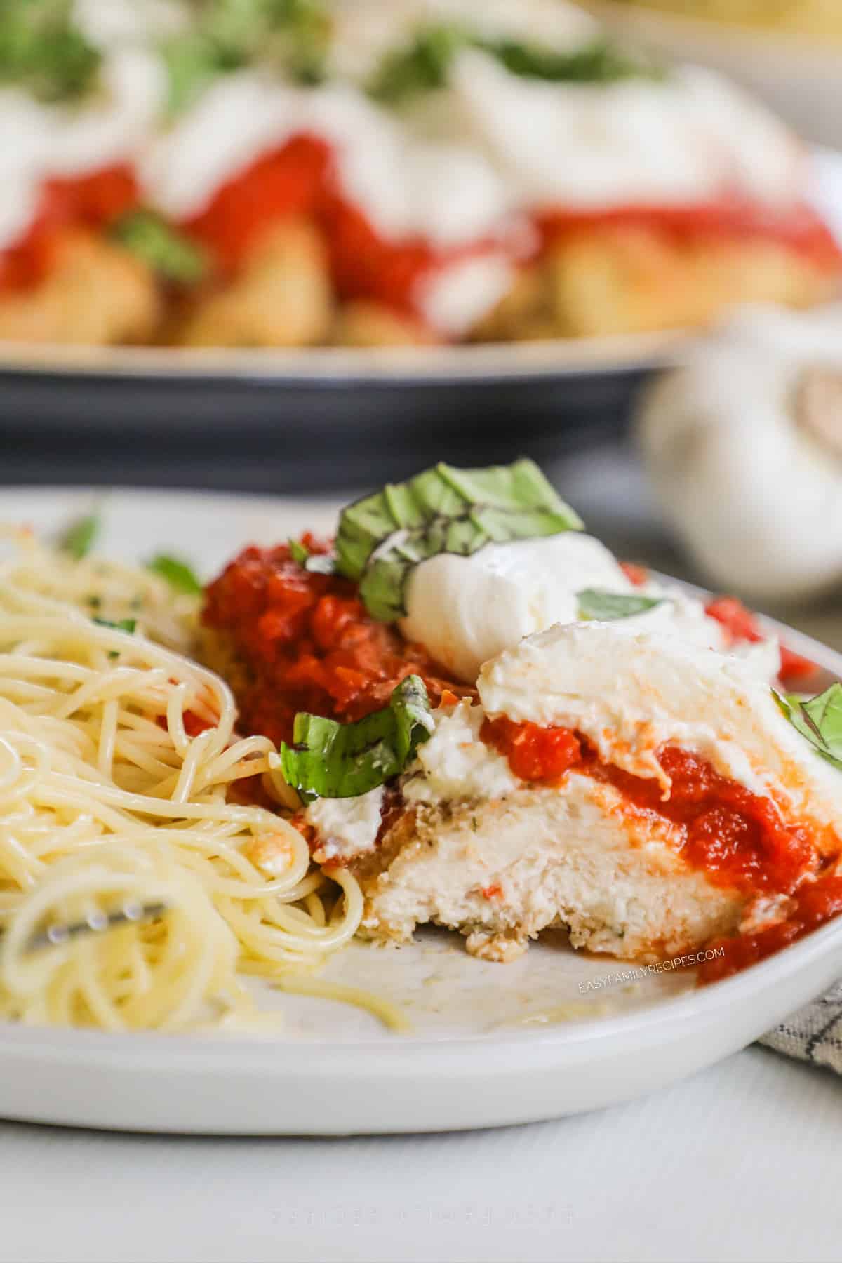 Burrata Chicken Parmesan with basil and pasta on a white plate.