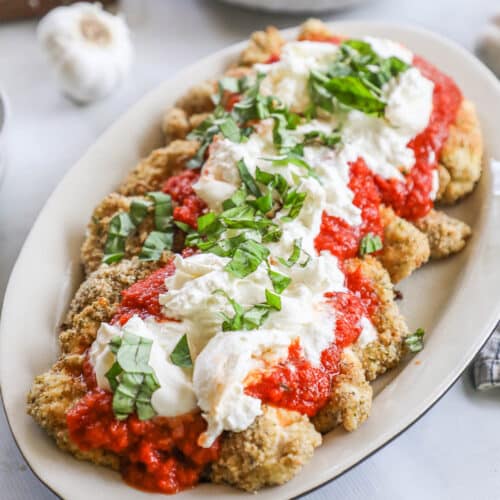 Burrata Chicken Parmesan on a white platter with garlic in the background.