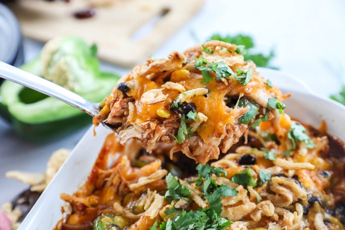BBQ Shredded Chicken Casserole being lifted out of the casserole dish with a spoon to serve for an easy dinner.