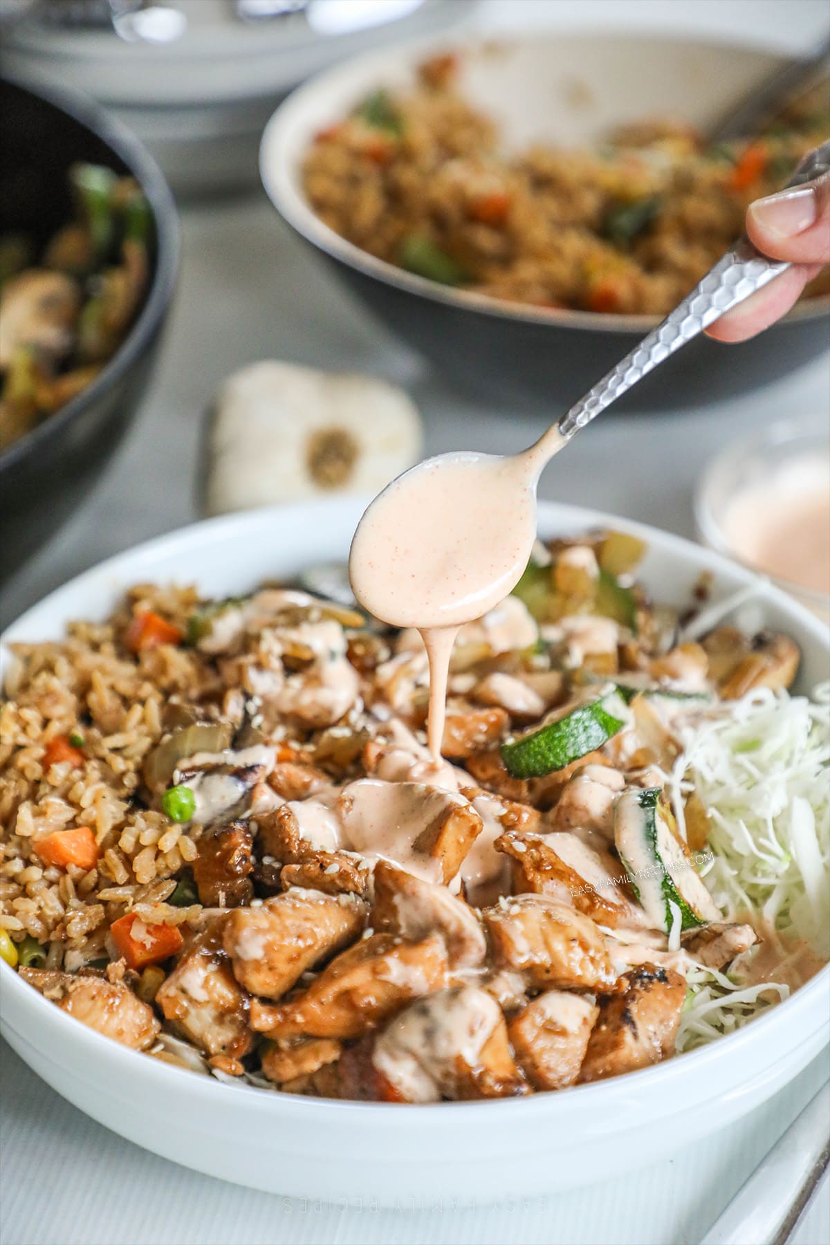 Hibachi chicken bowl served in a white bowl, with a silver spoon drizzling yum yum sauce over the top.