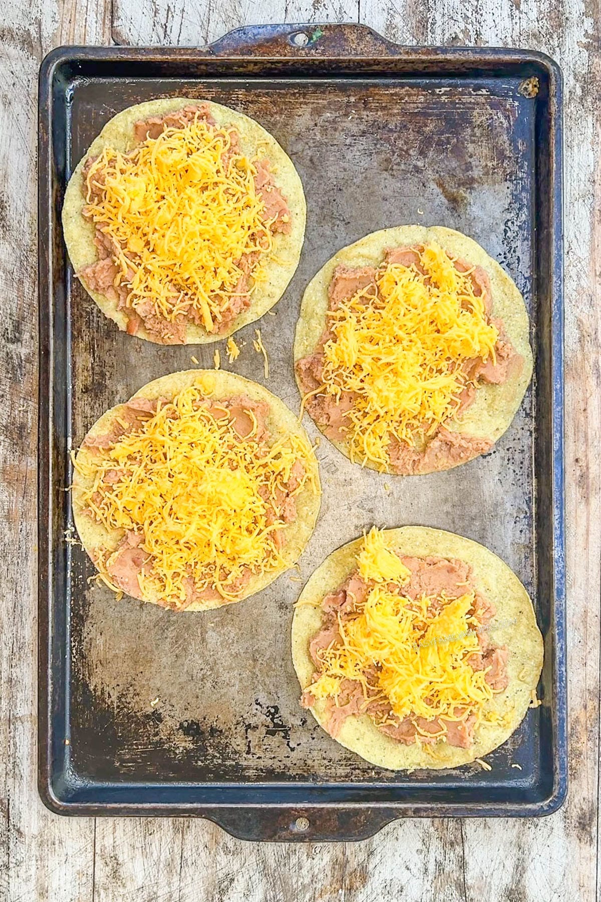 Cheese and refried beans on a tostada shell for BBQ chicken tostadas.