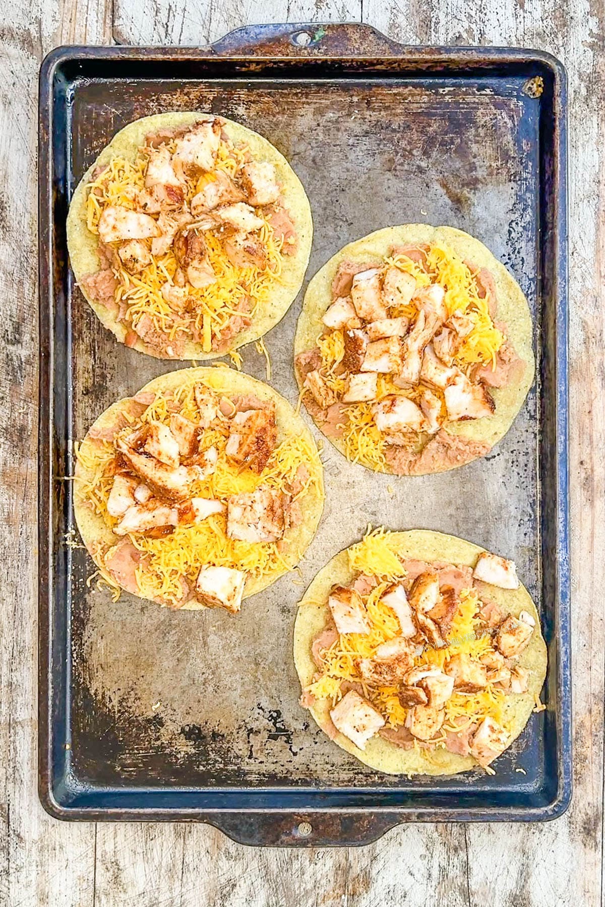 BBQ chicken is added to cheese and beans on a tostada shell for BBQ Chicken Tostadas.