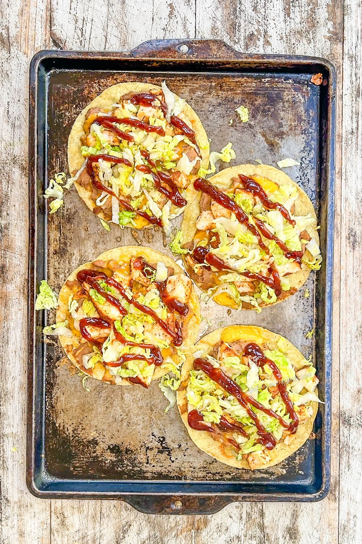 BBQ sauce is drizzled over BBQ chicken tostadas on a baking sheet.