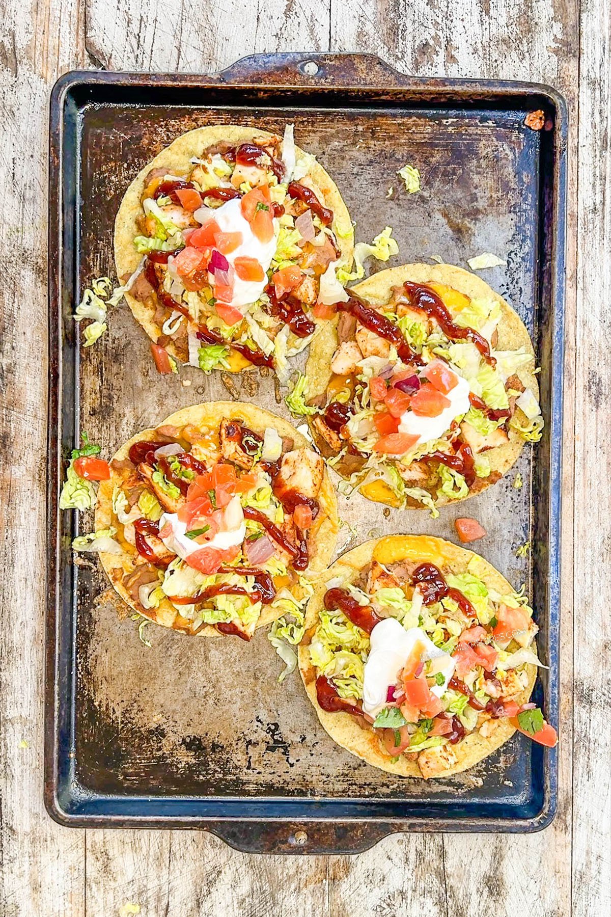 Toppings are added to BBQ chicken tostadas on a baking sheet.