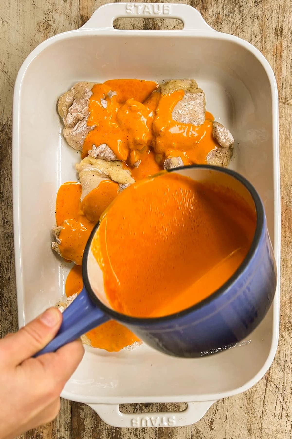 Sauce is poured over baked chicken thighs in a white casserole dish.