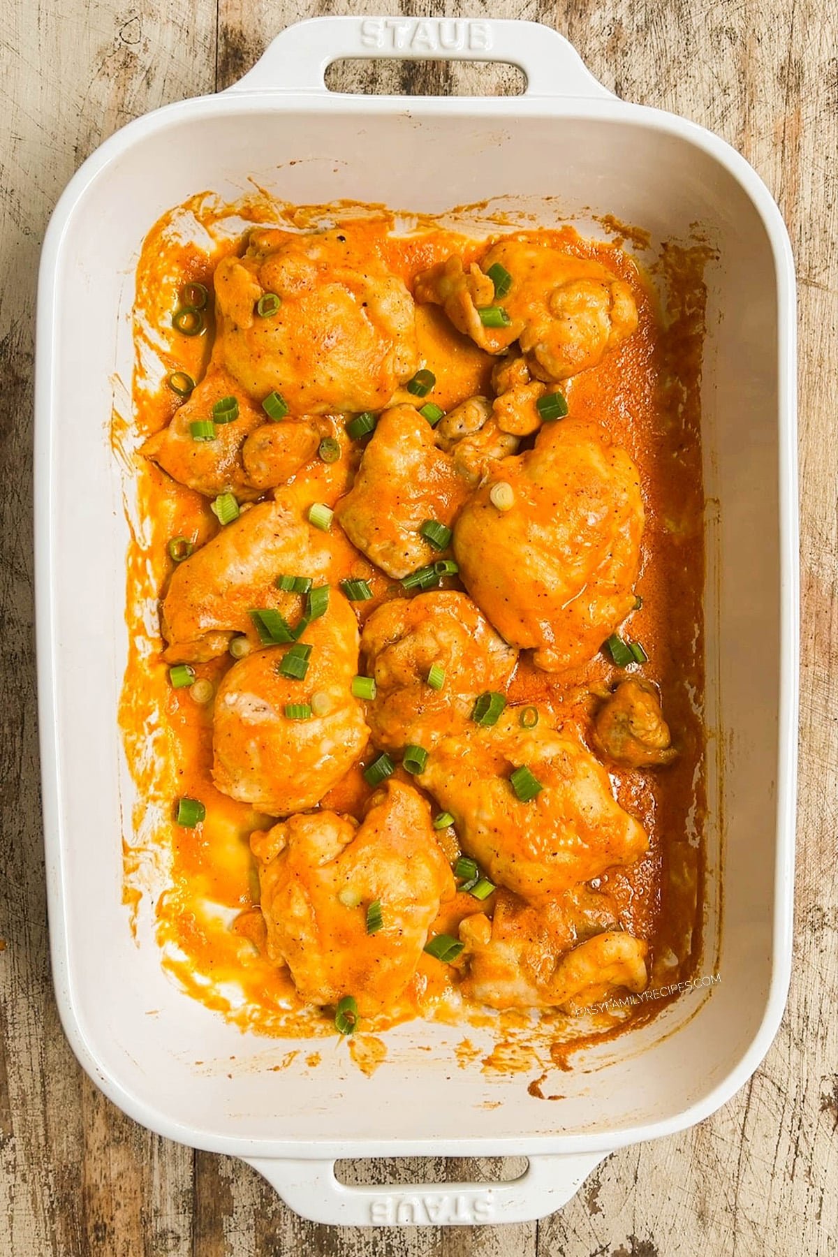 A top view of baked buffalo chicken thighs in a white casserole dish.