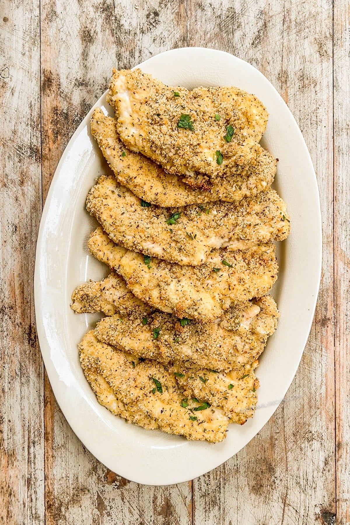 Chicken cutlets on a white oval platter for Burrata Chicken Parmesan.