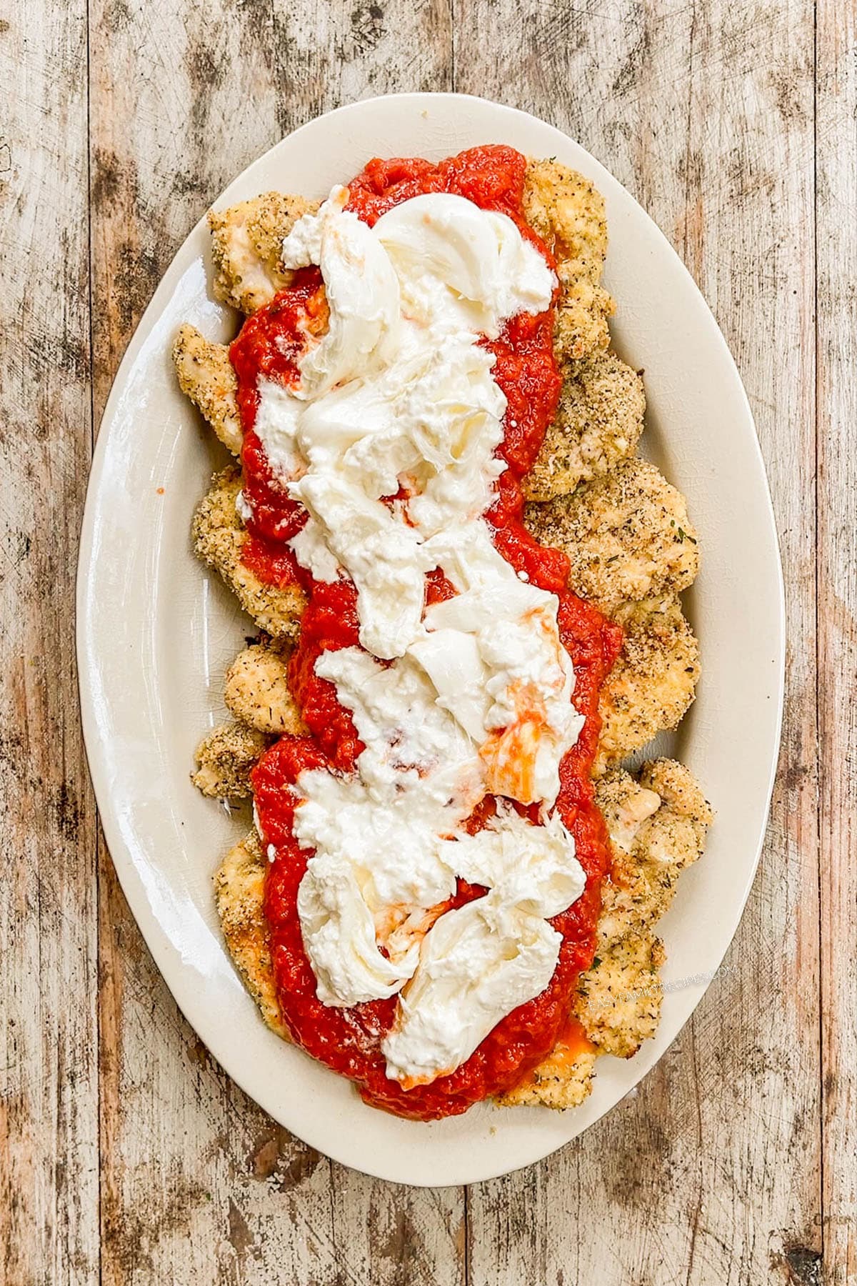 Torn burrata is placed over chicken and marinara for Burrata Chicken Parmesan.