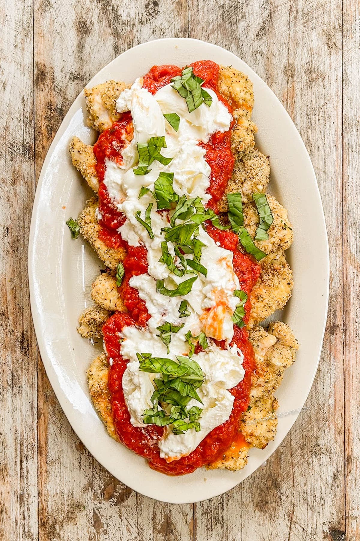 Fresh basil tops torn burrata and marinara sauce over baked chicken cutlets for for Burrata Chicken Parmesan.