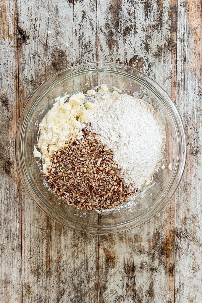 Step 3 to making Cinnamon Snowball Cookies - pecans and additional ingredients are added to the cookie batter in a glass bowl.