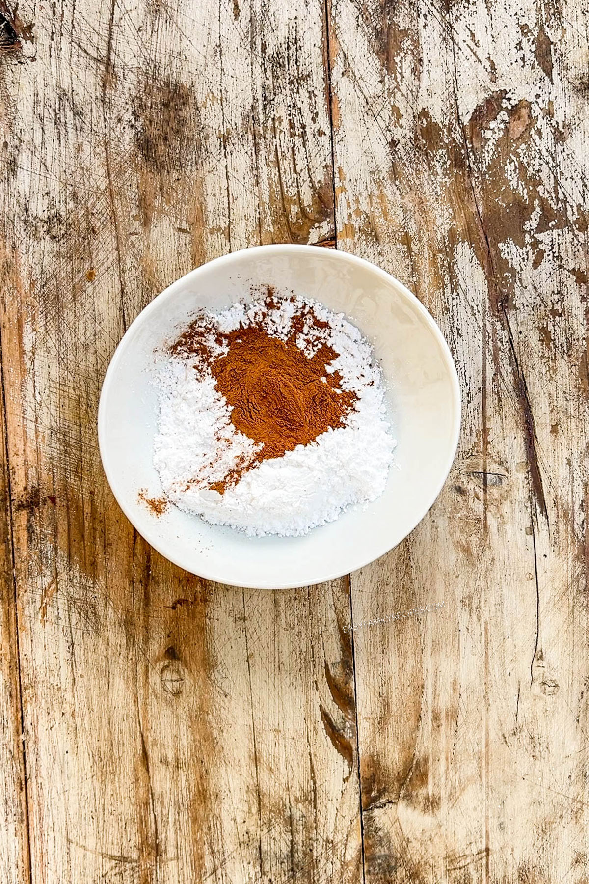 Cinnamon and powdered sugar are added to a bowl for cinnamon snowball cookies.