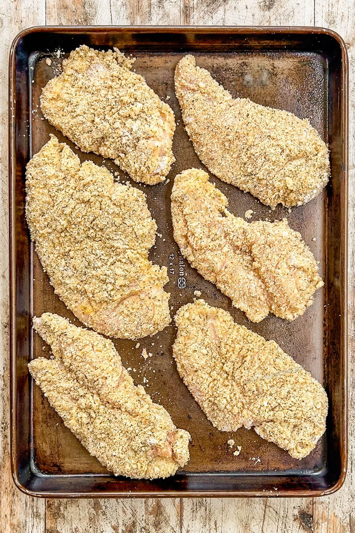 Breaded chicken on a baking sheet, ready to be baked.