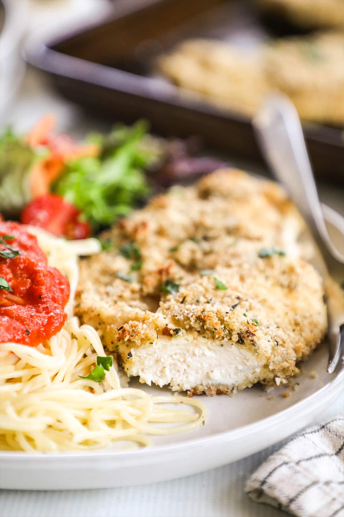 A white plate with a baked chicken cutlet, pasta, and sauce.