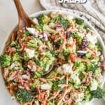 Top view of a white bowl full of broccoli salad with a wooden spoon. The text reads, "Broccoli Crunch Salad."