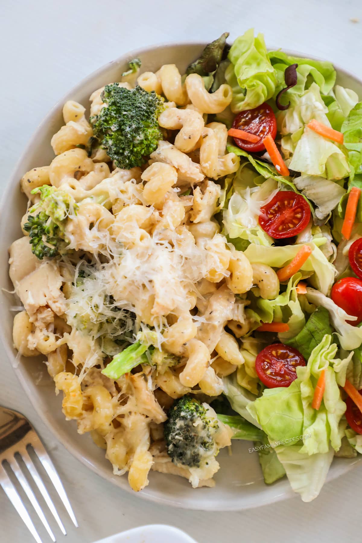 a pile of chicken broccoli alfredo on a plate with a side salad.