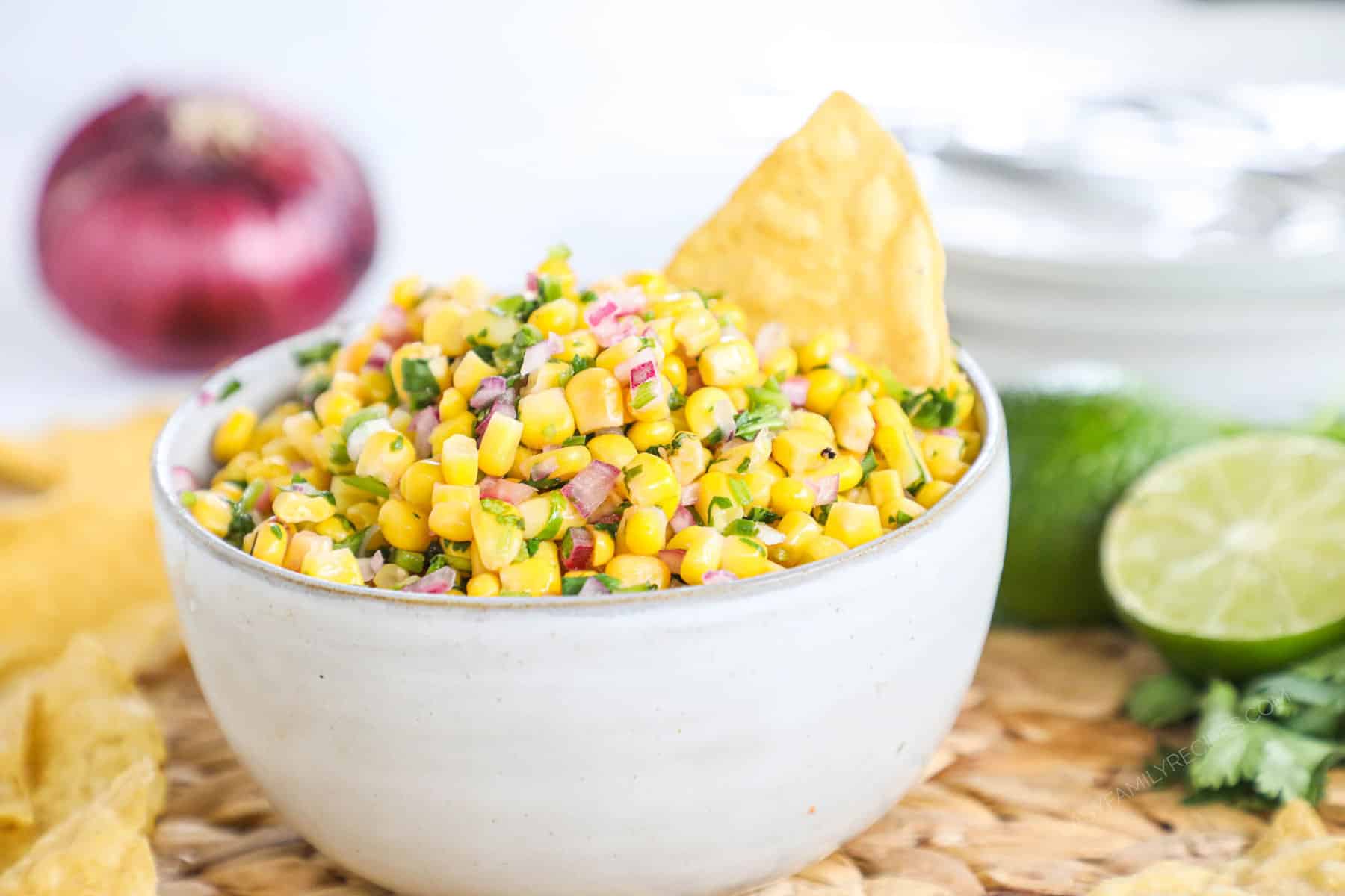 A white bowl of corn salsa and a chip