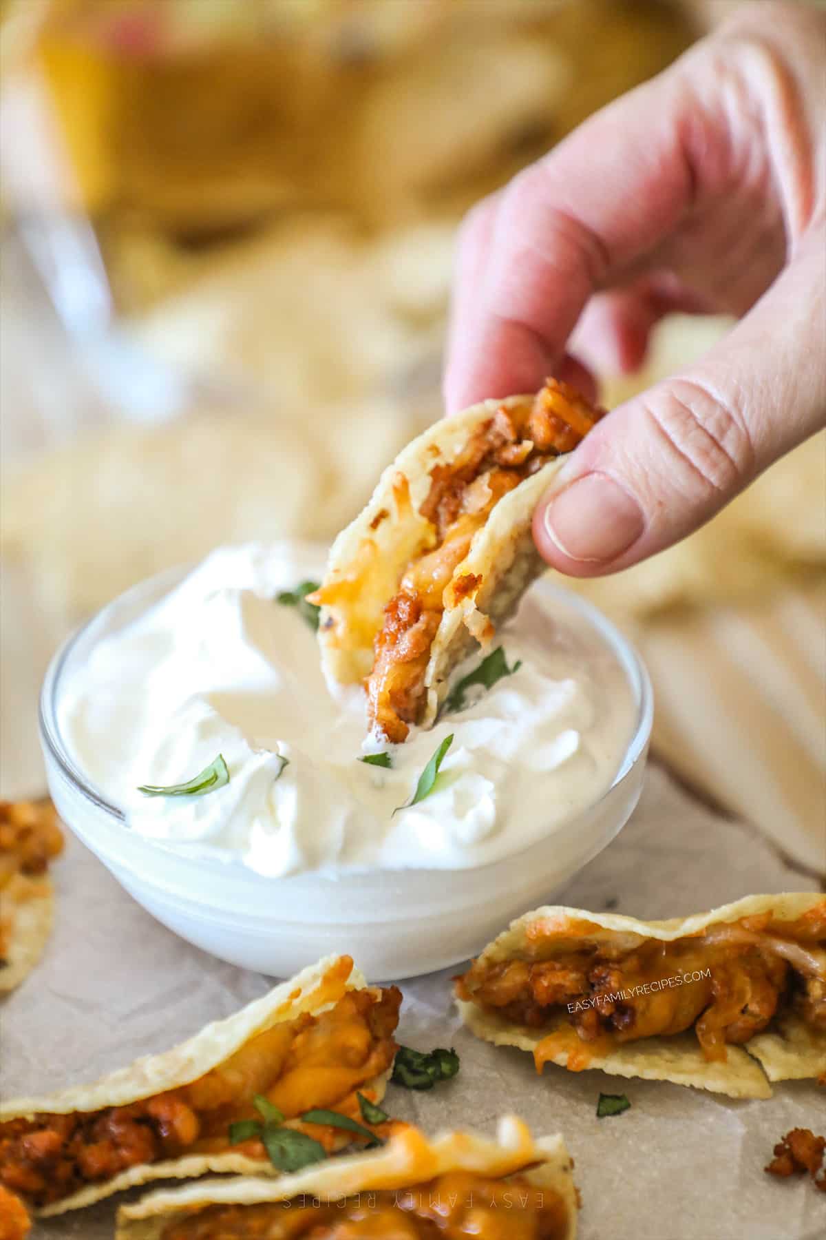 A hand dips a Tiny Taco into sour cream.