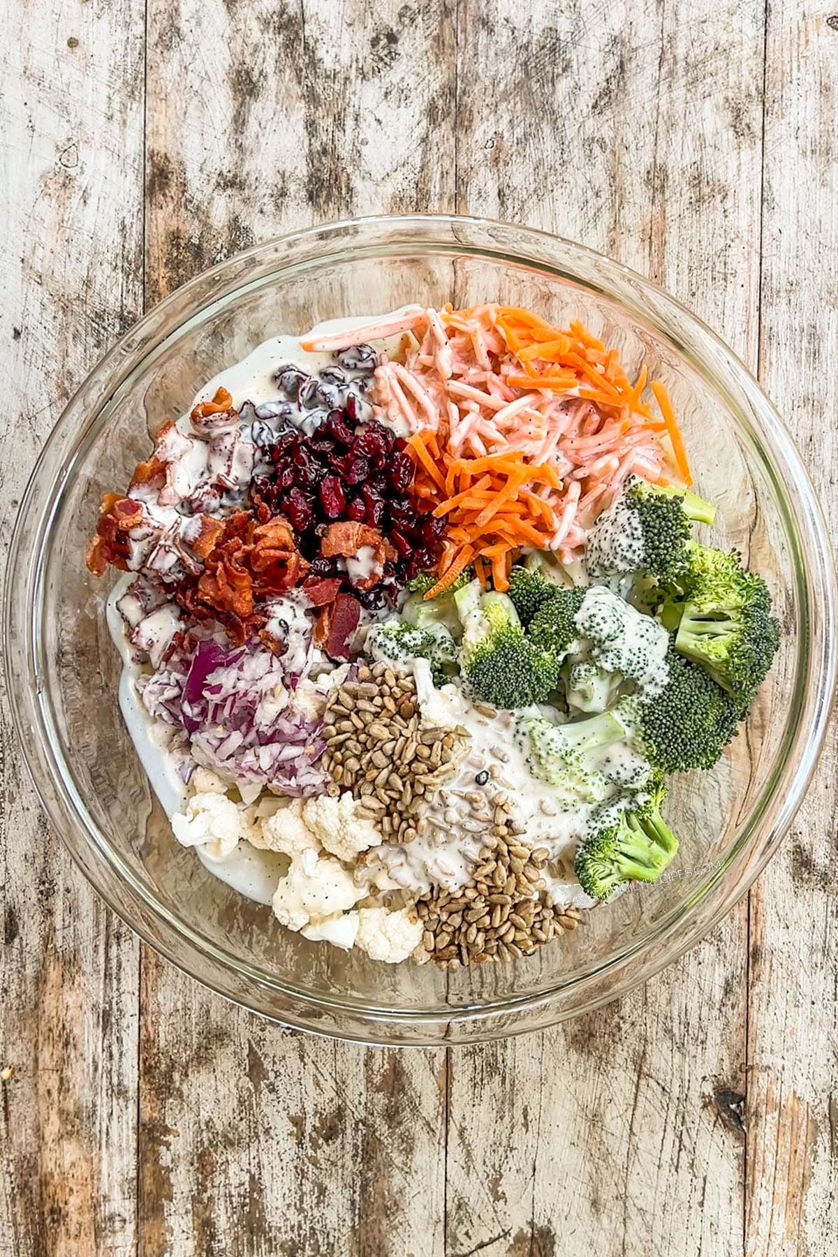 Dressing is poured over the ingredients in A white bowl filled with Broccoli Crunch Salad