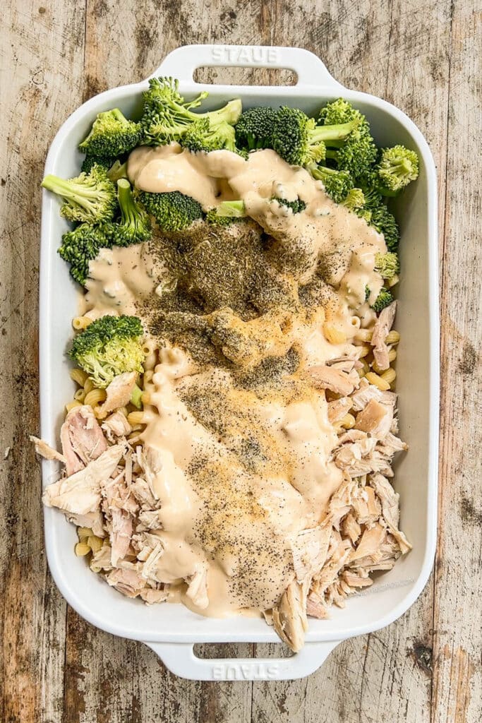 cooked pasta and broccoli in a baking dish topped with alfredo sauce and spices.