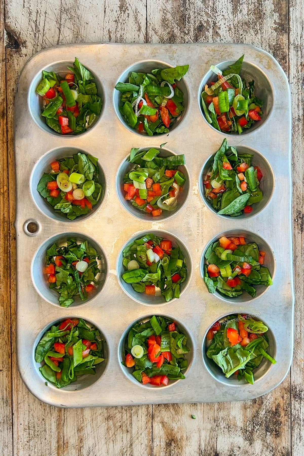 Red pepper and scallions are added to the muffin pan for cottage cheese egg bites.