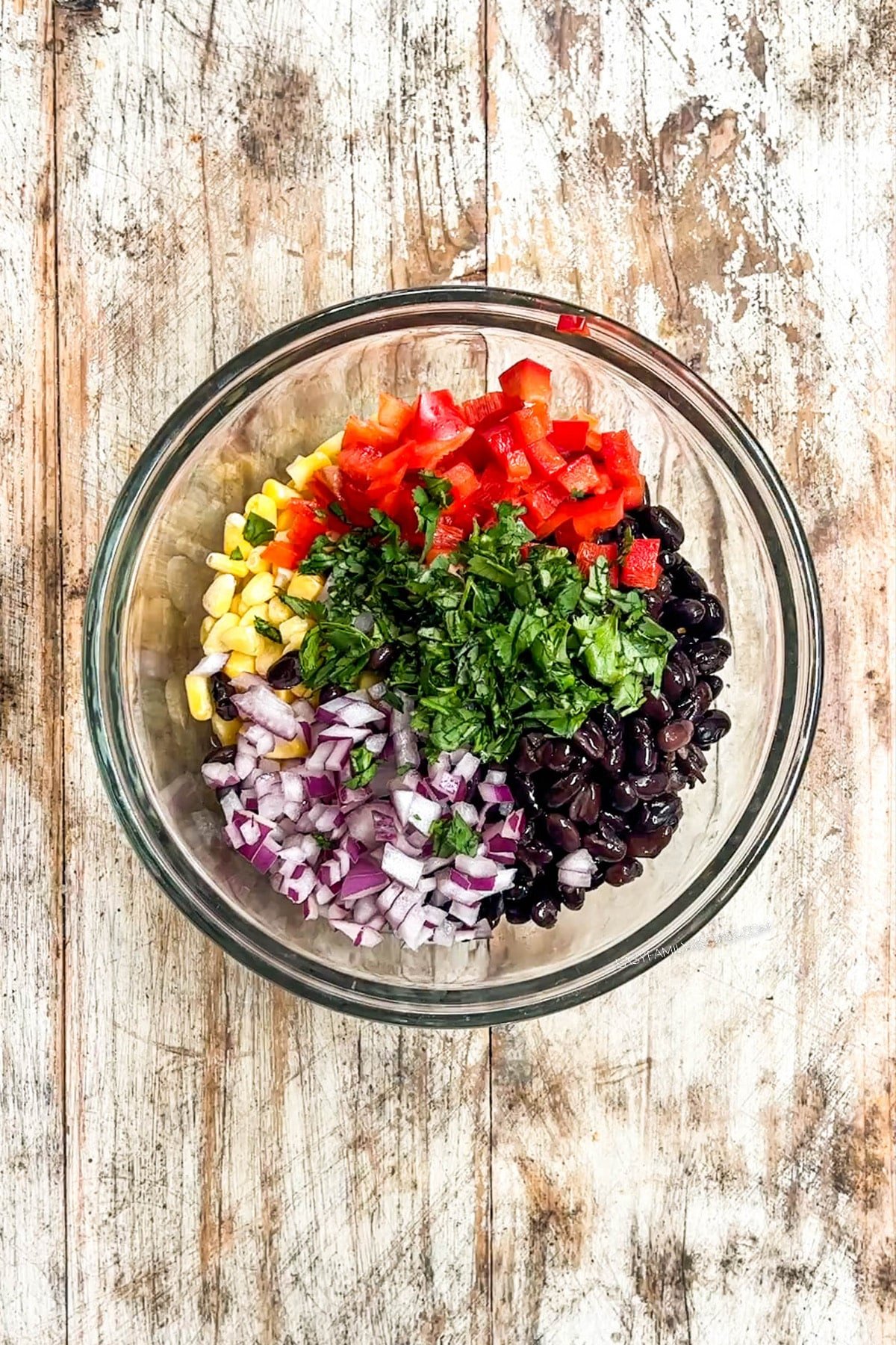 Black bean and corn salsa ingredients in a glass mixing bowl on a distressed wood background.