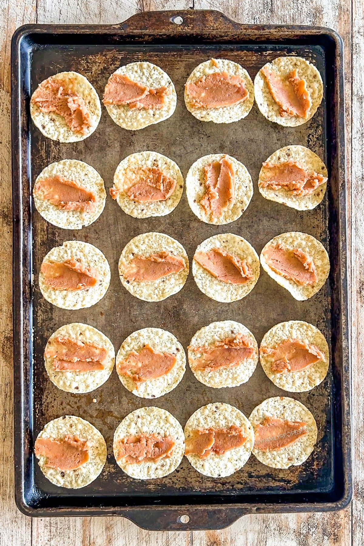 Step 1 of how to make Tiny Tacos - refried beans are spread onto round tortilla chips.