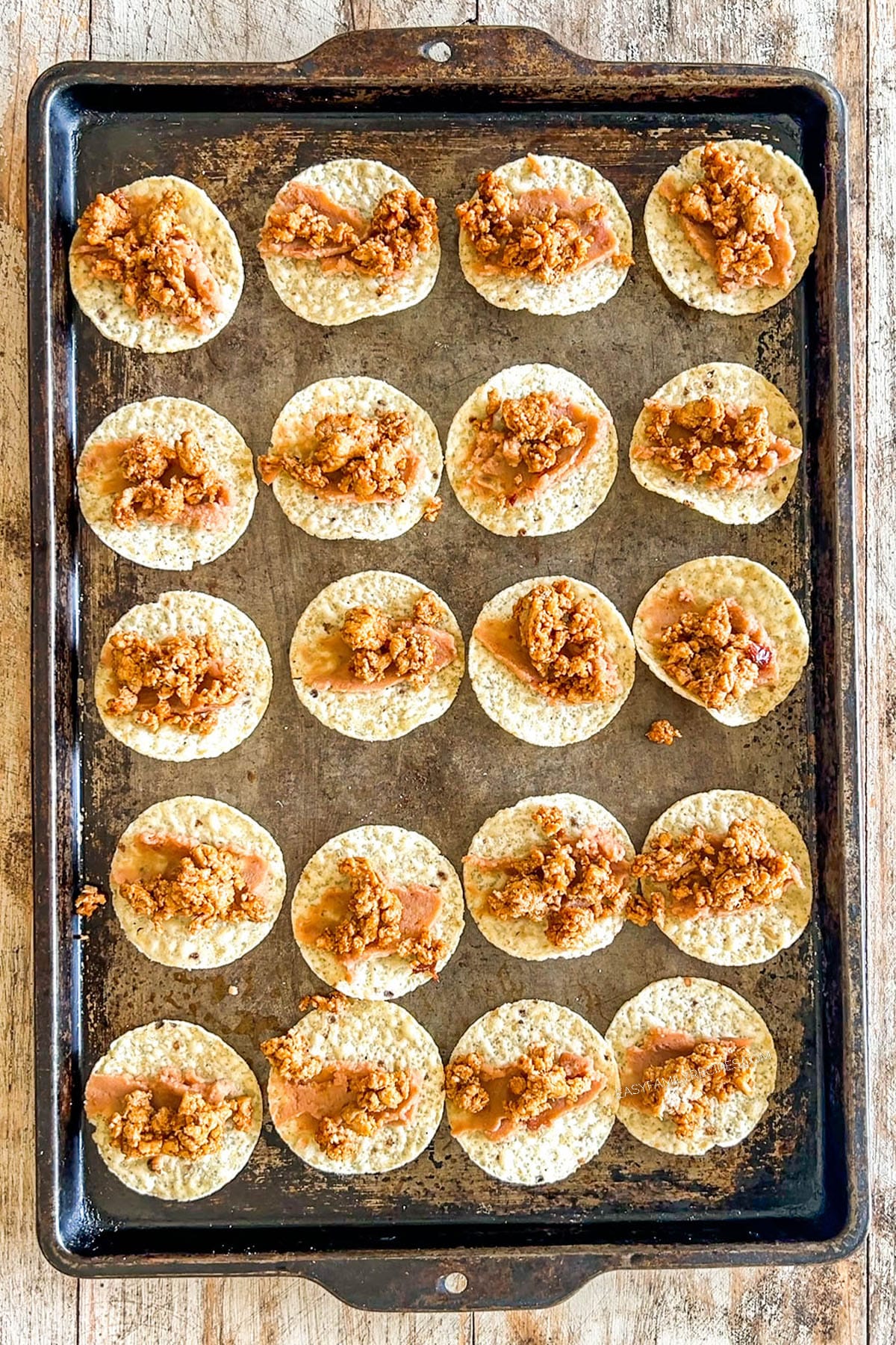 Step 2 of making Tiny Tacos - taco meat is added to the round tortilla chip on a metal baking sheet.