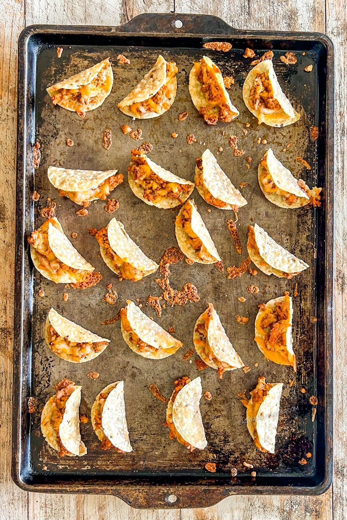 Rows of tiny tacos on a metal baking sheet.