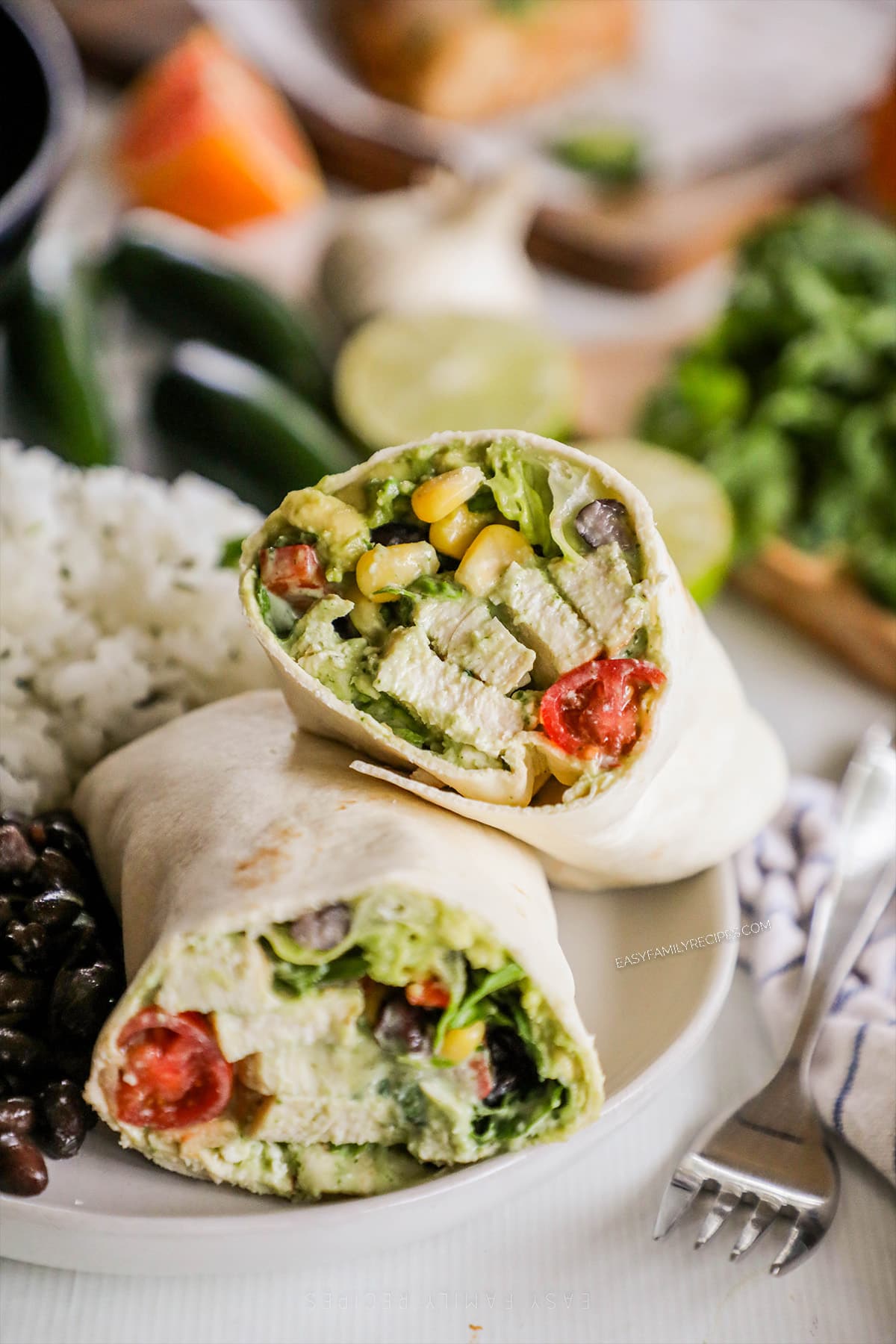 an assembled baja chicken wrap cut in half on a plate served with rice and beans.