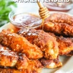 A white platter full of hot honey chicken tenders with fresh herbs. A honey dipper drizzles hot honey over the freshly fried chicken. The text reads, “Hot Honey Chicken Tenders”